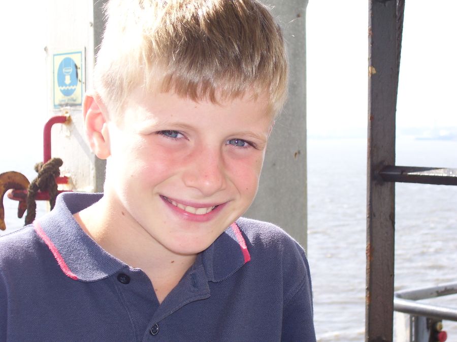 John as a boy, grinning by the water on a day out