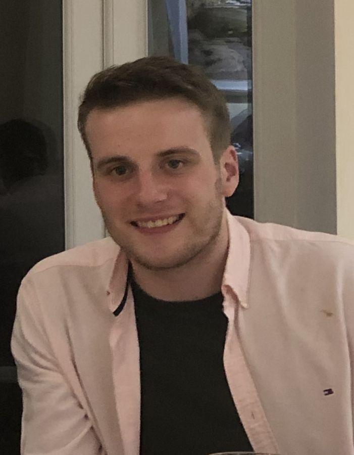 John as a young man in a pink shirt, smiling