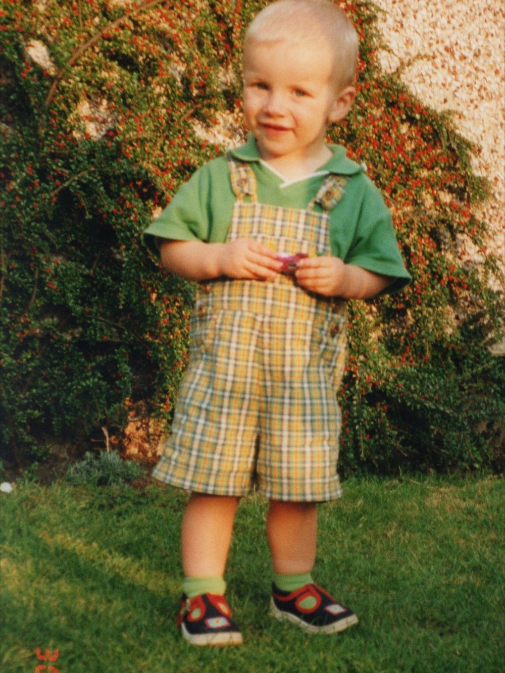 John as a small boy, standing in a garden in checked dungarees